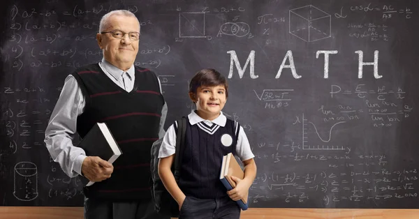 Schoolboy and an elderly male teacher posing in front of a black — Stock Photo, Image