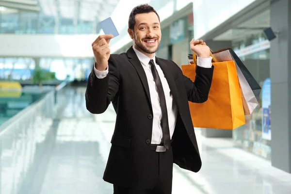 Uomo d'affari con borse della spesa che mostrano una carta di credito in un centro commerciale — Foto Stock