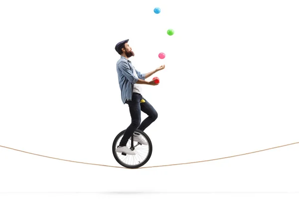 Bearded male hipster juggler with balls riding a unicycle on a r — Stock Photo, Image