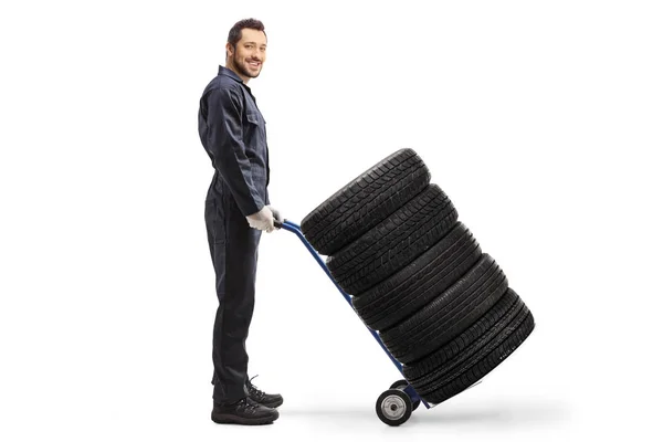 Man in een werkend uniform duwt een handtruck met autobanden — Stockfoto