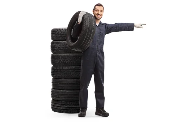 Auto mekaniker står bredvid en hög med däck, håller ett däck en — Stockfoto