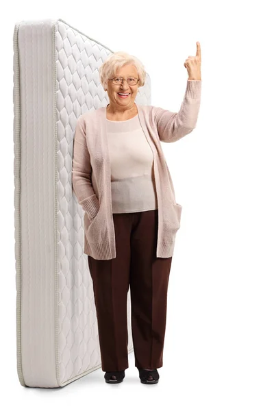 Elderly lady leaning on a bed mattress and pointing up — Stock Photo, Image