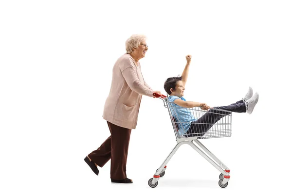 Grandmother pushing a shopping cart with a boy sitting inside — Stock Photo, Image