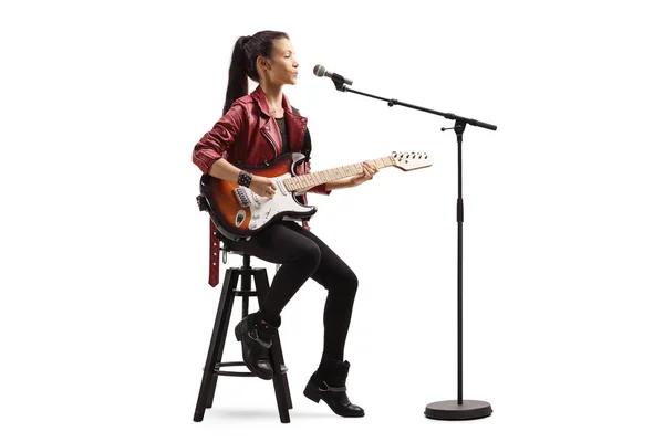Νεαρή γυναίκα παίζει κιθάρα και τραγουδάει σε μικρόφωνο — Φωτογραφία Αρχείου