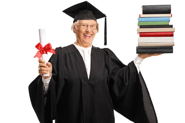 Senior woman in a graduation gown holding a diploma and a pile o — ストック写真