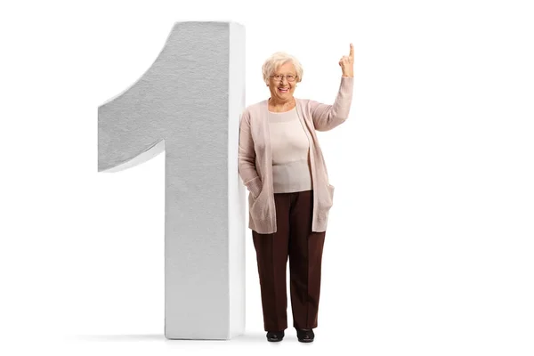 Donna anziana appoggiata a un grande numero uno e che punta sopra — Foto Stock