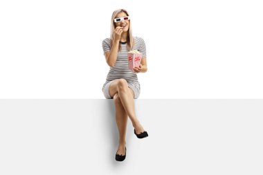 Bir kutu patlamış mısırla boş bir panelde oturan kadın.