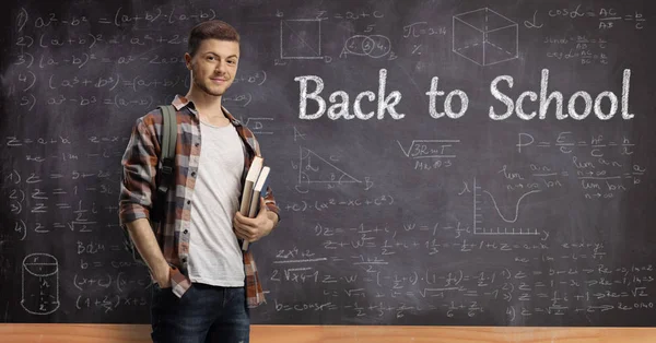 Estudiante masculino con libros delante de una pizarra con t —  Fotos de Stock