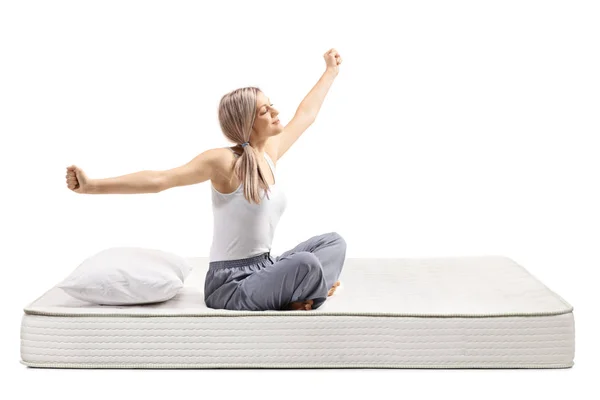 Jonge vrouw in pyjama zitten op een bed matras en stretching — Stockfoto