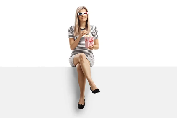 Young blond woman sitting on a panel eating popcorn and wearing — 스톡 사진