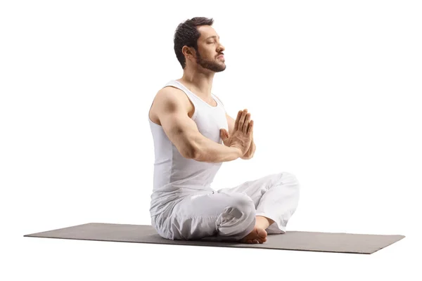 Joven sentado en una alfombra de ejercicio en una pose de meditación —  Fotos de Stock