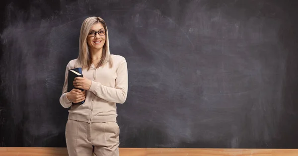 Giovane insegnante di sesso femminile davanti a una lavagna e con libri in mano — Foto Stock