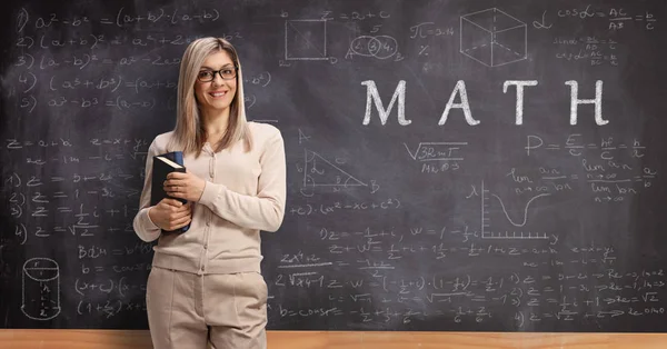 Young female teacher standing in front of a blackboard with text — Stock Photo, Image