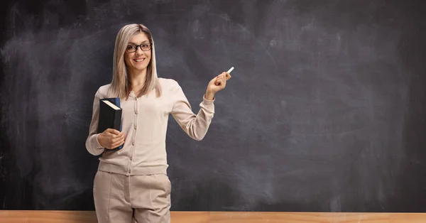 Jonge vrouwelijke professor voor een schoolbord en het houden van een ch — Stockfoto