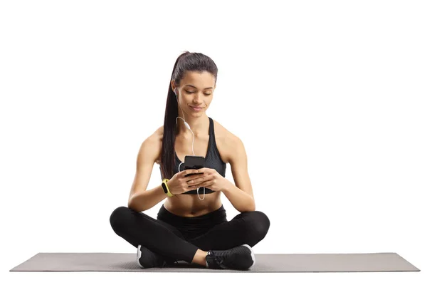 Young female with earphones and phone sitting on an exercise mat — Stock Photo, Image