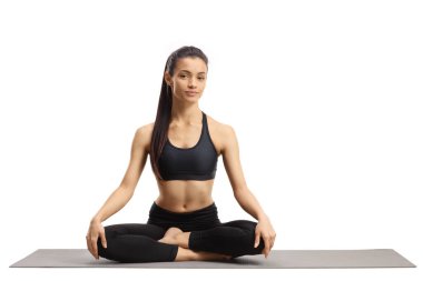 Spor kıyafetli genç bir kadın bacak bacak üstüne atmış bir mindere oturuyor. 