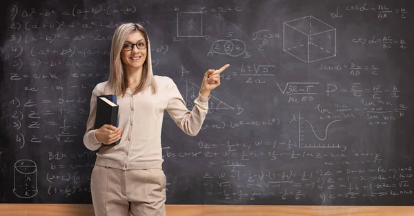 Giovane insegnante di sesso femminile che punta su una lavagna scuola con la matematica f — Foto Stock