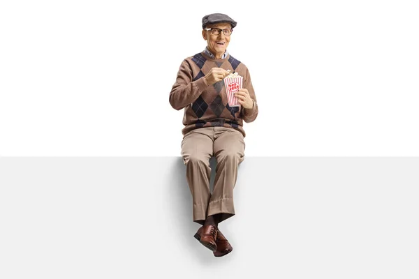Starší muž sedí na panelu a jí popcorn a mele v Camer — Stock fotografie