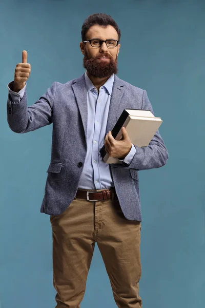 Gözlüklü sakallı adam kitap tutuyor ve başparmağını kaldırıyor. — Stok fotoğraf