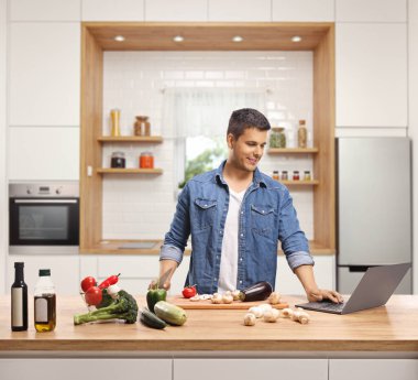 Young man cooking in a kitchen with a laptop