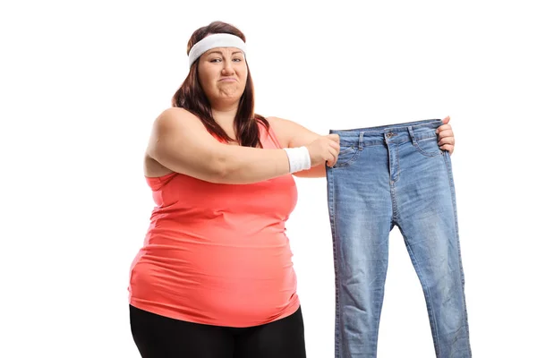 Smutna kobieta z nadwagą w odzieży sportowej trzymająca parę małych dżinsów — Zdjęcie stockowe