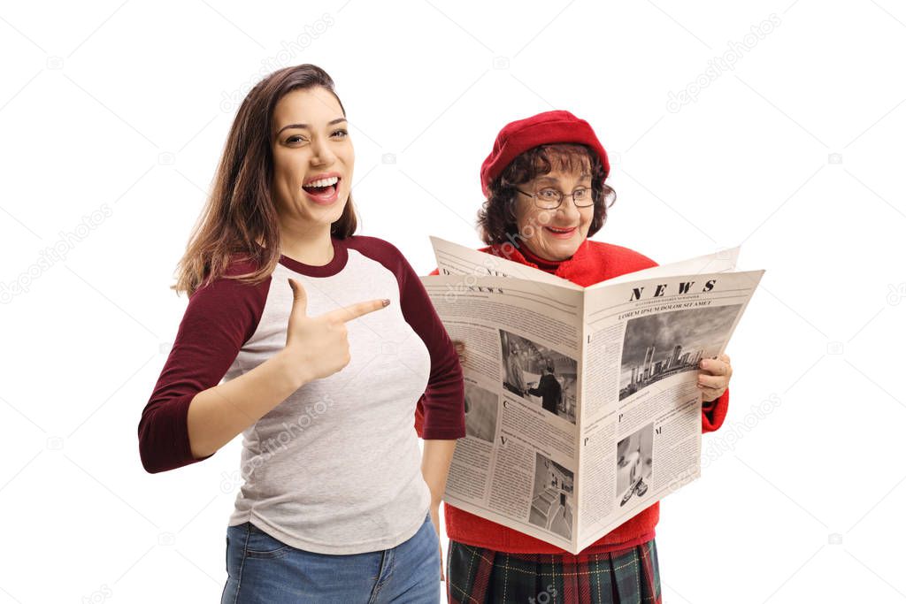 Young female laughing and pointing at a senior woman reading a n