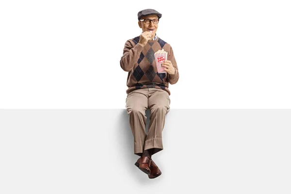 Homme âgé souriant et assis sur un panneau avec du pop-corn — Photo
