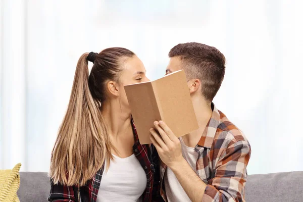 Young male and female kissing behind a book — Stock Photo, Image