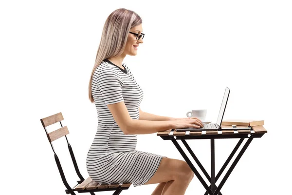 Wanita muda duduk di meja dan bekerja pada laptop di kafe — Stok Foto
