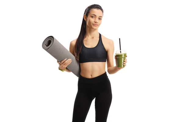 Spor kıyafetli genç bir kadın elinde yeşil bir milkshake ve bir egzersiz tutuyor. — Stok fotoğraf