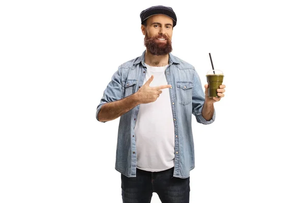 Бородатий молодий хлопець з чашкою зеленої смузі вказує — стокове фото