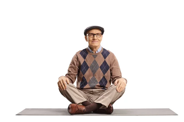 Elderly man sitting on a mat with crossed legs — Stockfoto
