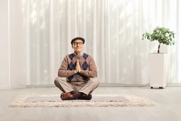 Uomo anziano seduto su un tappeto con le gambe incrociate meditando — Foto Stock
