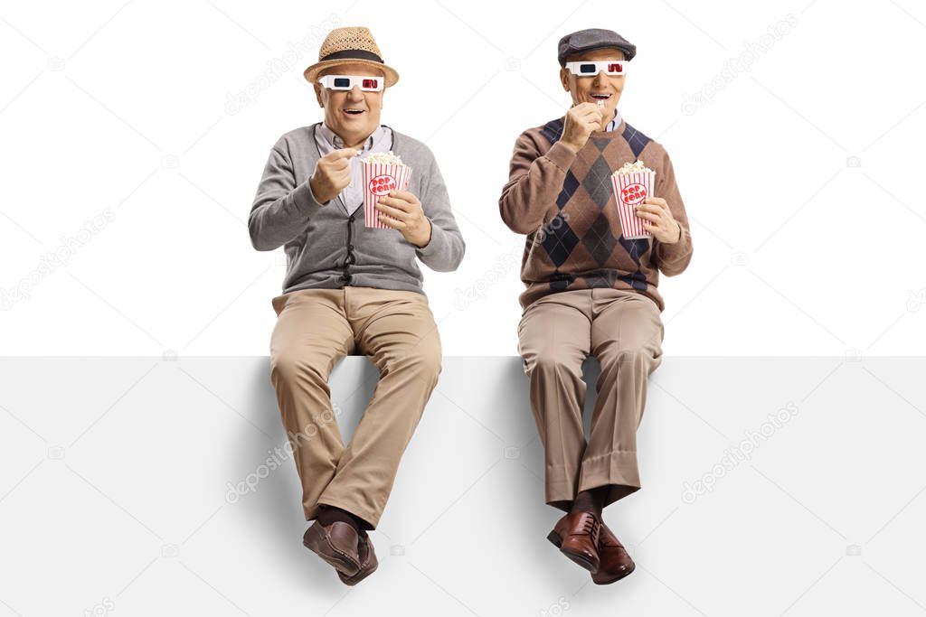 Two senior men sitting on a panel eating popcorn and watching a 