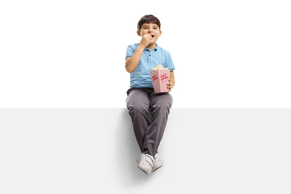 Cute boy sitting on a panel and eating popcorn — Stok fotoğraf