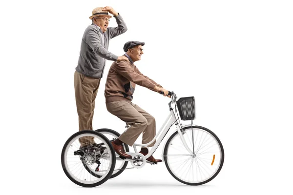 Idoso montando um triciclo e um cavalheiro sênior de pé ser — Fotografia de Stock