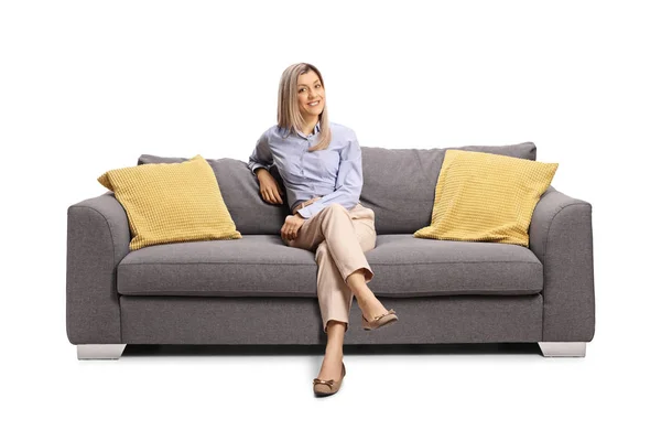 Jovem mulher sentada em um sofá e sorrindo — Fotografia de Stock
