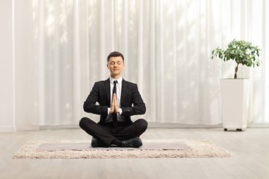 Genç işadamı bacak bacak bacak üstüne atmış ve evde meditasyon yapıyor.