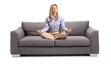 Resmi kıyafetli genç bir kadın kanepeye oturmuş, bacak bacak bacak üstüne atmış, meditasyon pozu vermiş, beyaz arka planda izole edilmiş.