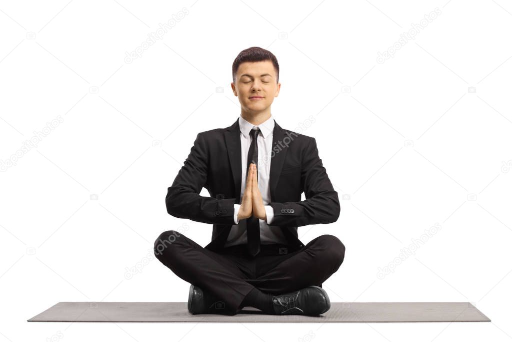 Young man in a black suit with closed eyes sitting with crossed legs and meditating isolated on white background