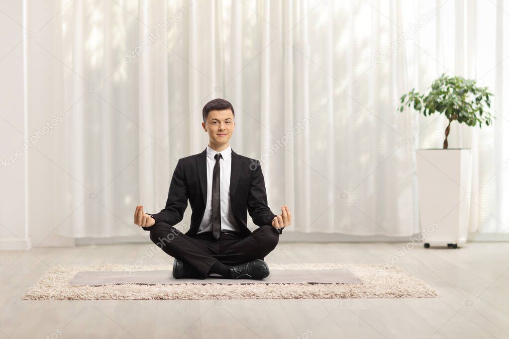 Elegant man in a black suit sitting on the floor and exercising yoga at home 