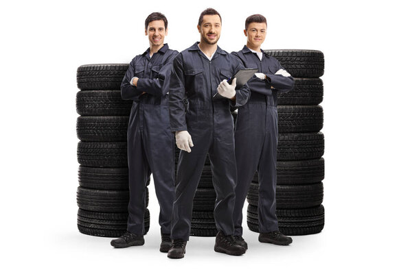 Full length portrait of a team of mechanics standing with piles of tires isolated on white background