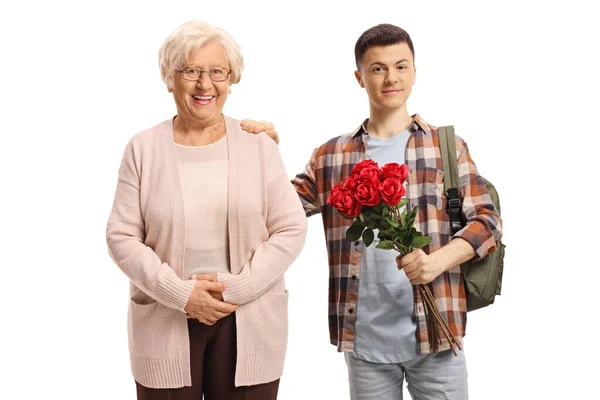10代の男子学生は赤いバラの束を保持し 白の背景に隔離された高齢者の女性の隣に立って — ストック写真