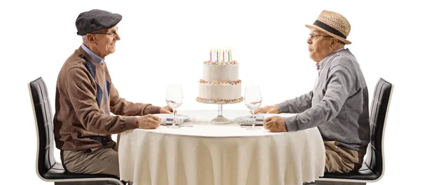 白い背景に隔離されたケーキの上にろうそくを吹くテーブルの上に上級男性 — ストック写真