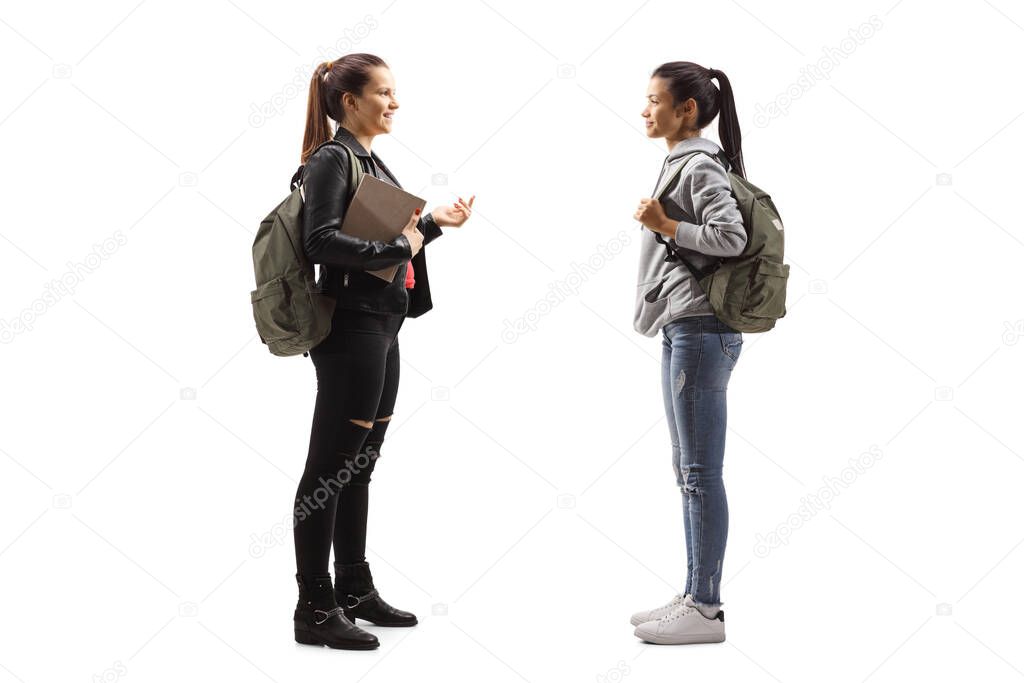 Full length profile shot of two female students talking isolated on white background