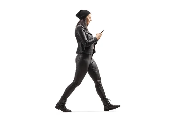 革の服の女性の完全な長さのプロフィールショット歩くと白の背景に隔離された携帯電話を見て — ストック写真