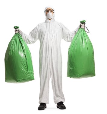 Beyaz arka planda plastik çöp torbaları taşıyan dezenfekte kıyafeti giymiş bir adamın tam boy portresi.