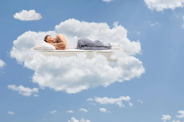 Man in pajamas sleeping on a mattress and floating in the sky surrounded by clouds