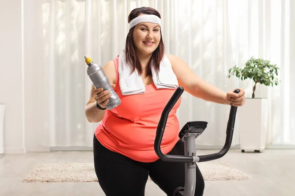 家で運動する静止自転車の上の太りすぎの若い女性 — ストック写真
