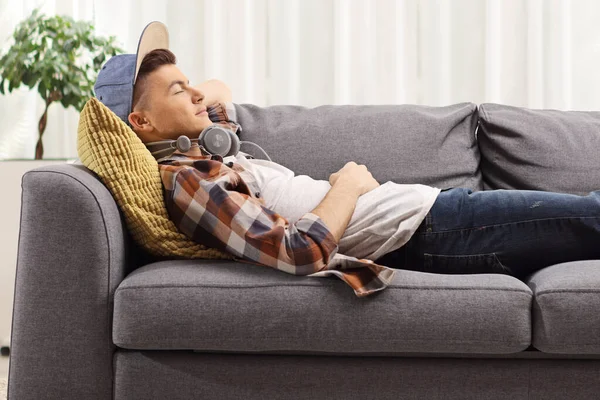 男性ティーン寝ています上のソファとともにヘッドフォンで自宅 — ストック写真